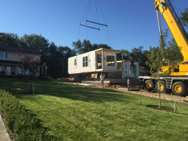 Crane lifting a modular section of a house set up on a construction site.